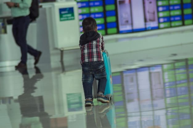 Passengers walking through an airport terminal, some pulling luggage, with flight information screens visible in the background. The scene depicts a smooth and efficient travel experience.