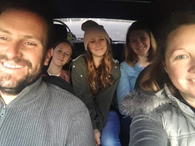 A family standing next to their newly acquired car, all smiling and looking at the camera. The scene emphasizes the positive impact of accessible transportation on family life.