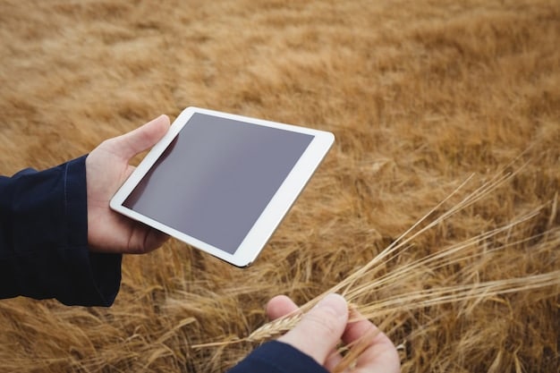 Close-up of a farmer's hands holding a digital tablet, displaying agricultural data charts, with a blurred background of a wheat field.