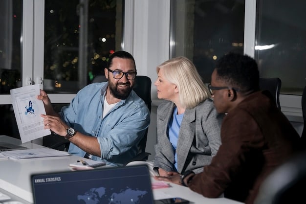 A diverse group of people in business attire discussing plans around a table in a brightly lit conference room. Charts and graphs are visible on a screen in the background.