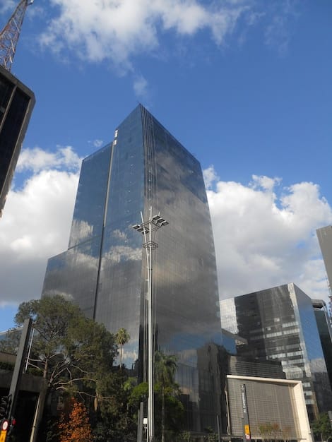 A close-up of the Brazilian Central Bank building with a determined sun and serious sky, with complex economic graphs superimposed and focusing. The numbers on the graphs suggest changes in interest rates, and the overall ambiance is one of economic strength and complexity.